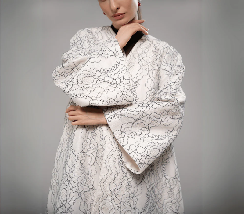 Elegant white embroidered abaya with delicate floral lace patterns from F.Lounge.Mena, showcasing modern modest fashion inspired by Dubai style